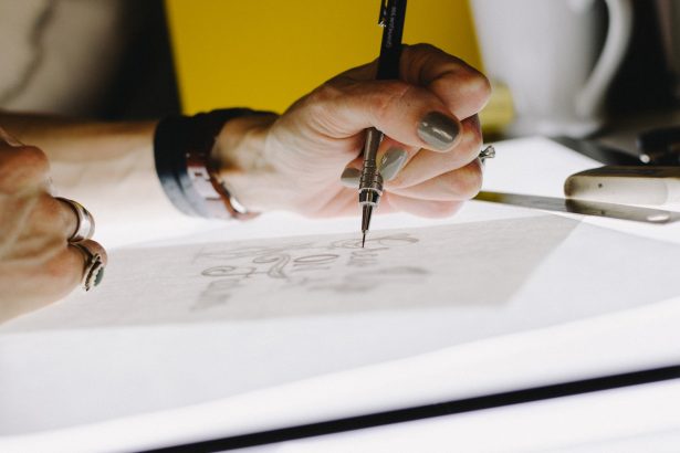 person lettering on tracing paper using mechanical pencil